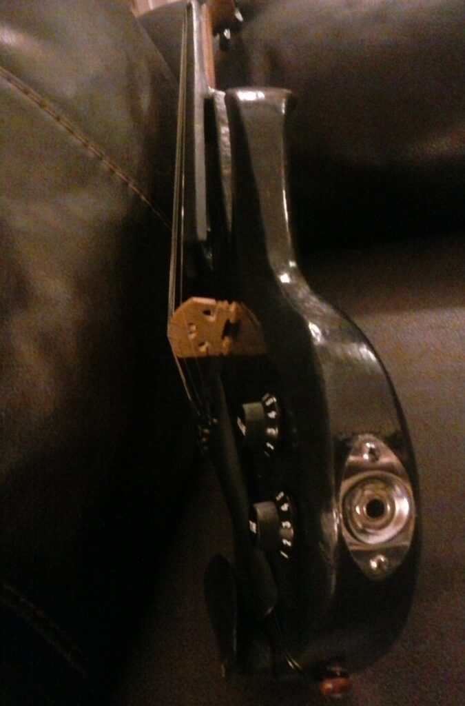 Stratocaster inspired electric violin built and hand-carved from scratch out of red oak, a passive piezo pickup and other electric components, guitar tuning pegs. Black in color.