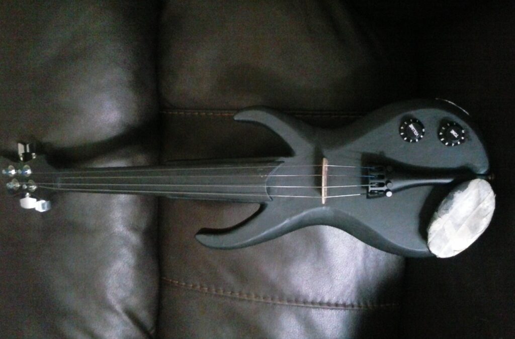 Stratocaster inspired electric violin built and hand-carved from scratch out of red oak, a passive piezo pickup and other electric components, guitar tuning pegs. Black in color. Unpainted.