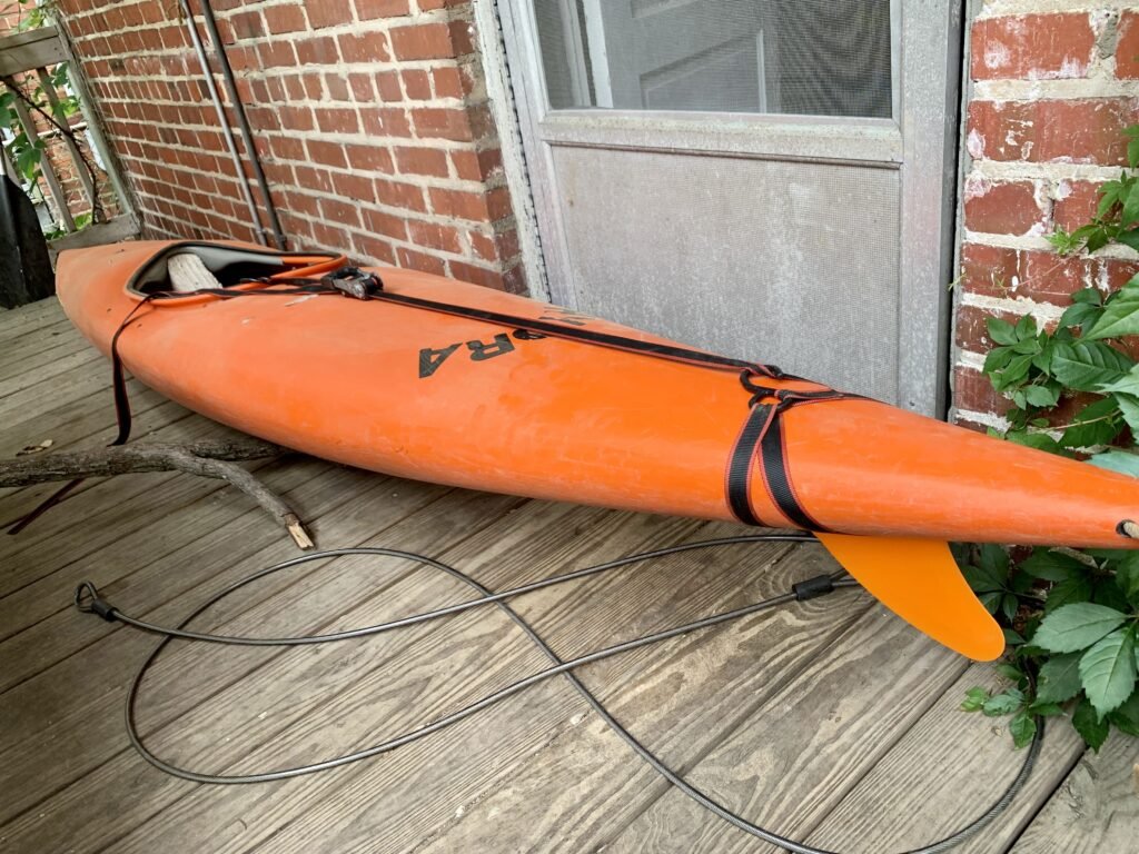 Orange whitewater Hydra kayak with the orange 3D modeled and 3D printed fin that requires you to ratchet strap it to the hull. 