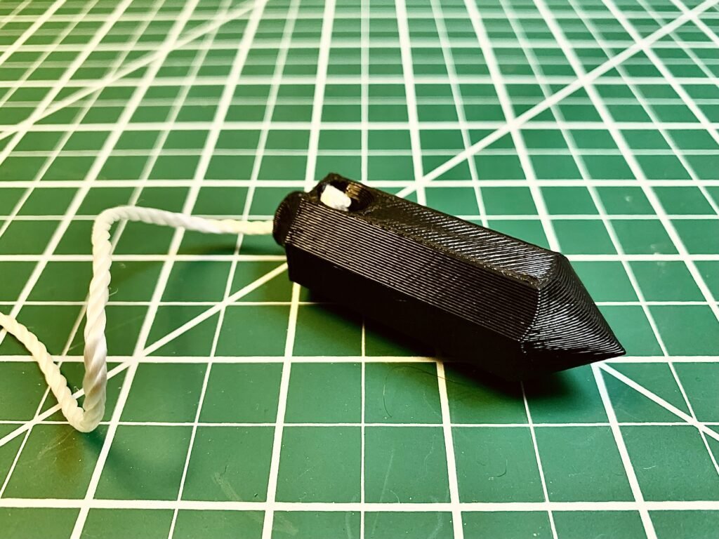 3D printed plumb bob, black with a string attached to one end. 