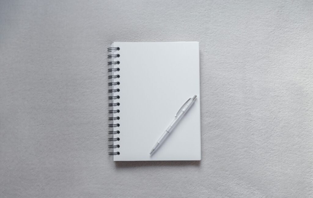 Photo by Diana Polekhina on Unsplash. A school, office notebook with a white pen lies on a gray table, desk, background. Place for an inscription. Office. Job. School. Personal diary. Top view.